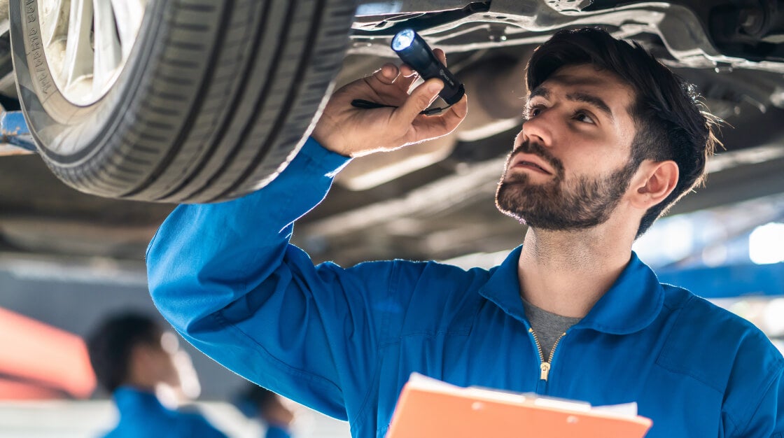 Man under a raised vehicle inspecting tire