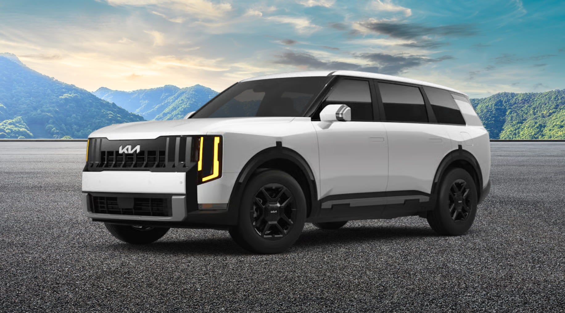 A white Kia Telluride SUV with black accents is parked on a textured surface with a backdrop of distant green mountains under a bright blue sky.
